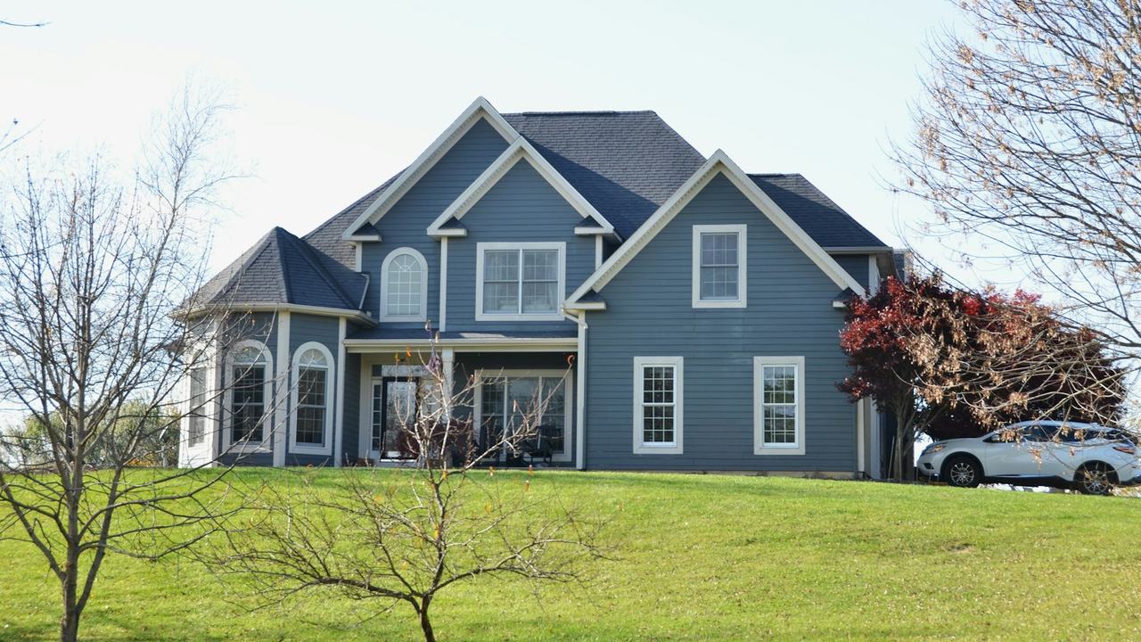 A blue two-storey house on a grassy lot in late autumn.