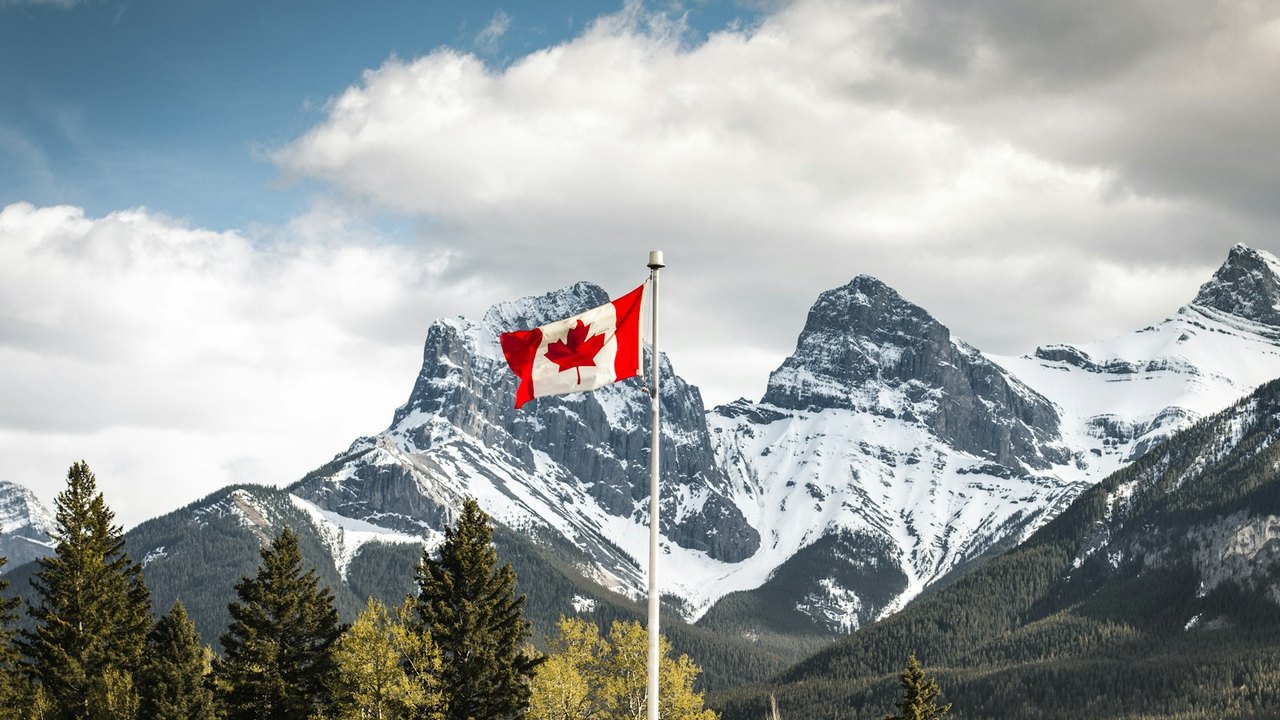 A Canadian flag flying in front of the Three Sisters peaks near Canmore, Alberta.