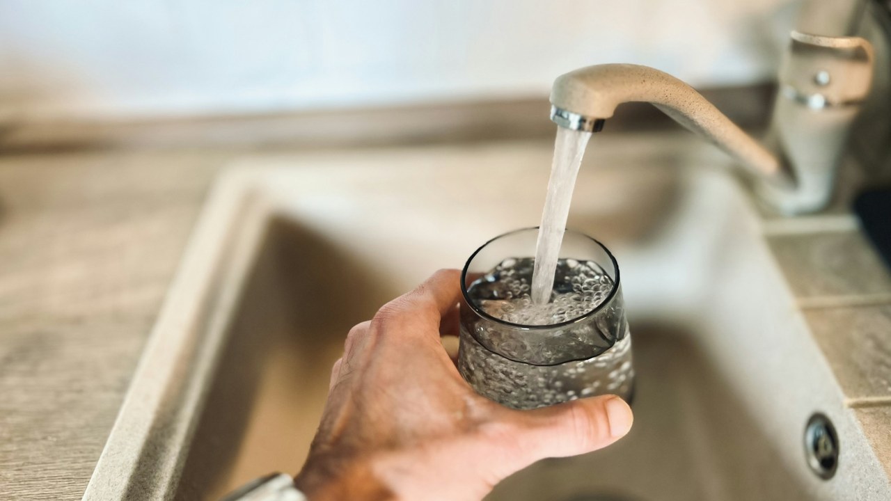 A hand filling a glass under a running kitchen tap.