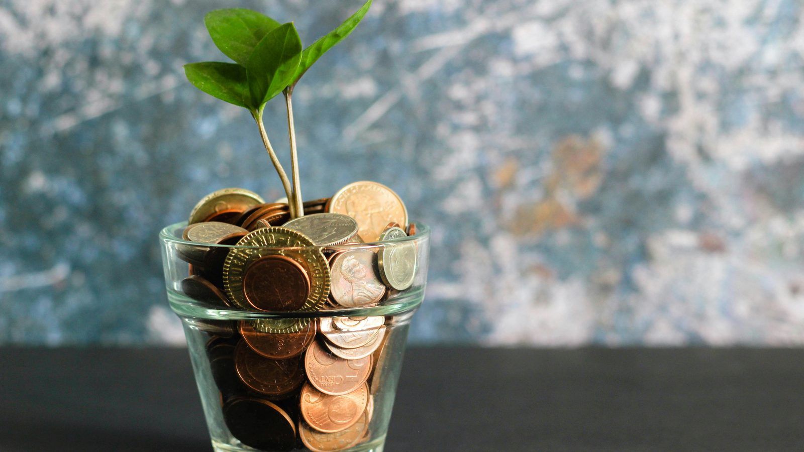 A glass jar of coins on a sunlit windowsill — saving for a first home, kept in plain view.