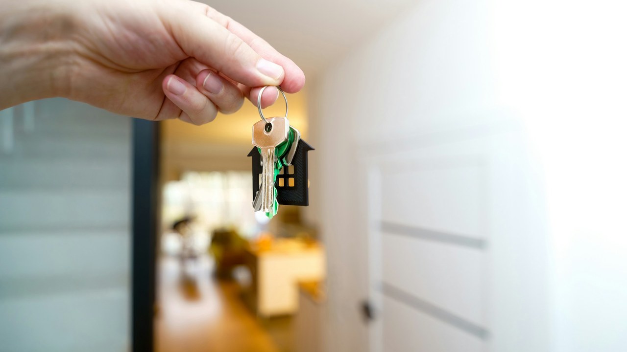 A hand holding up a set of house keys in a bright hallway.