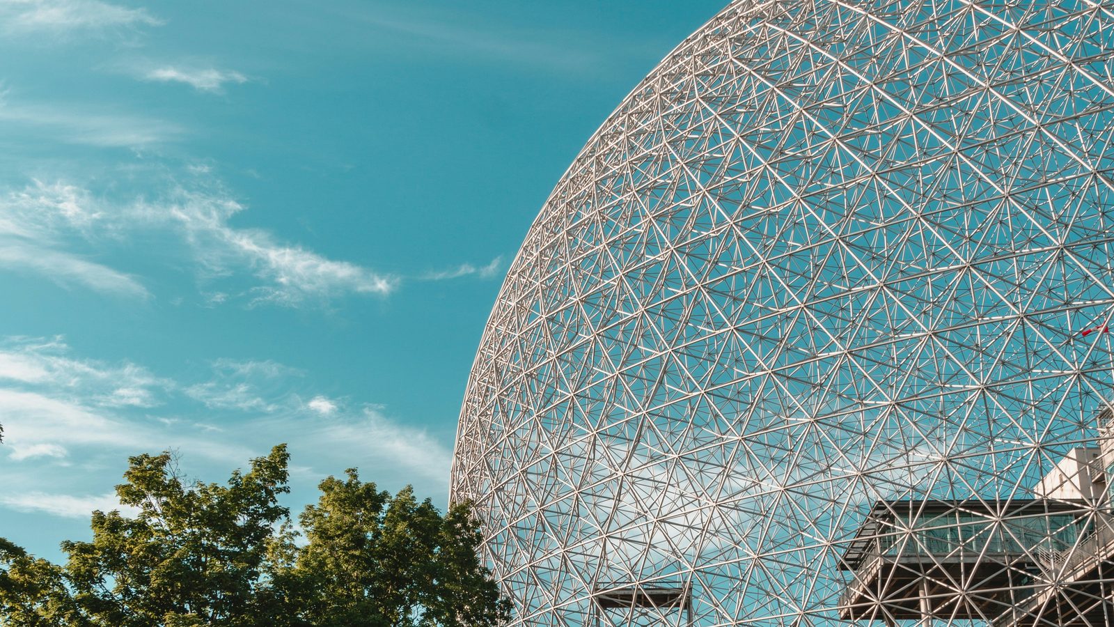 The geodesic dome of Montréal's Biosphère against a soft summer sky, framed by trees.