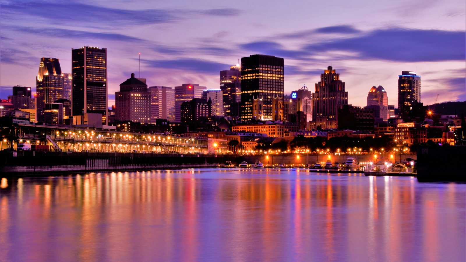 Montréal's downtown skyline glows at dusk, lights reflected across the St. Lawrence River.