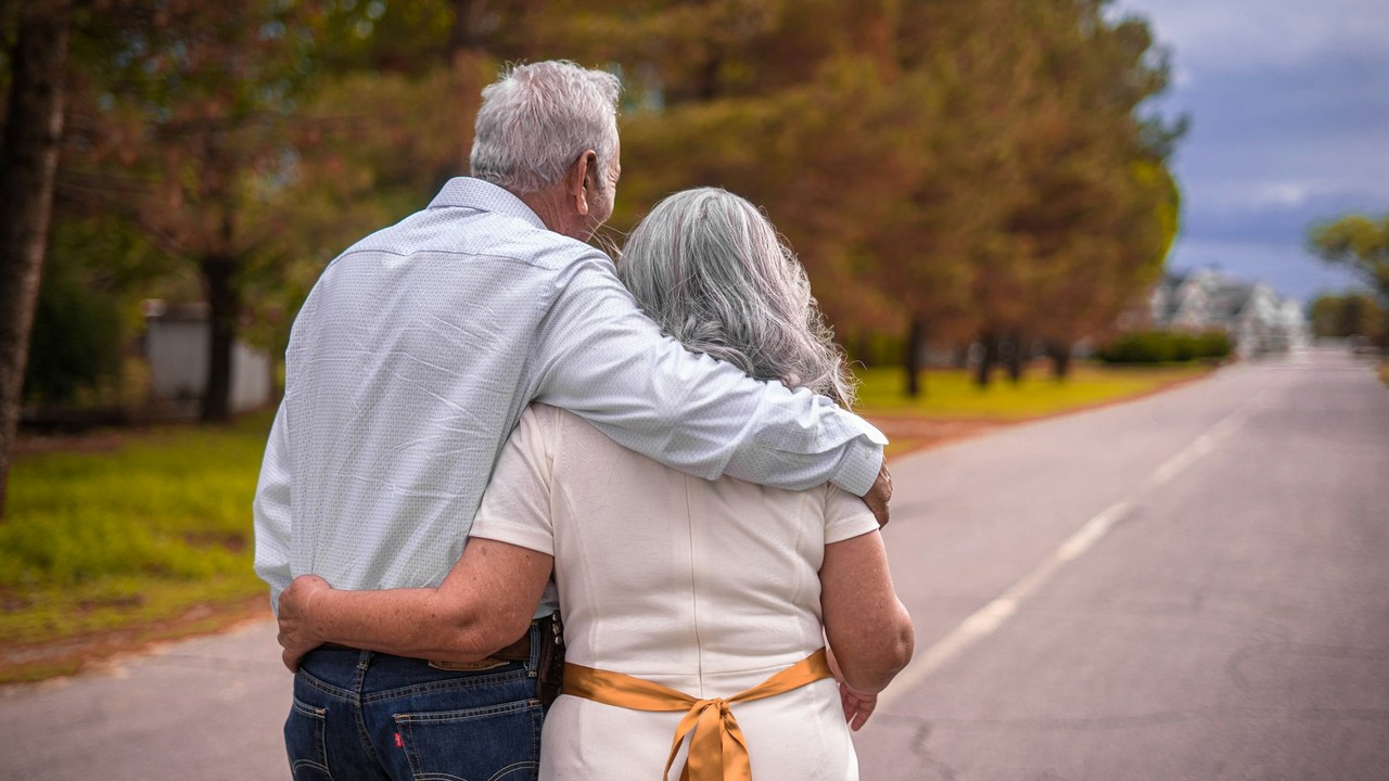 An older couple standing arm in arm on a quiet road.