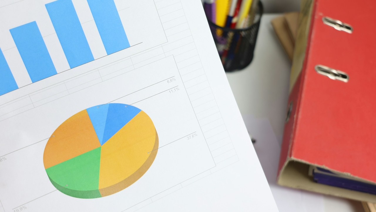 A printed report with a bar chart and a pie chart, next to a red binder.