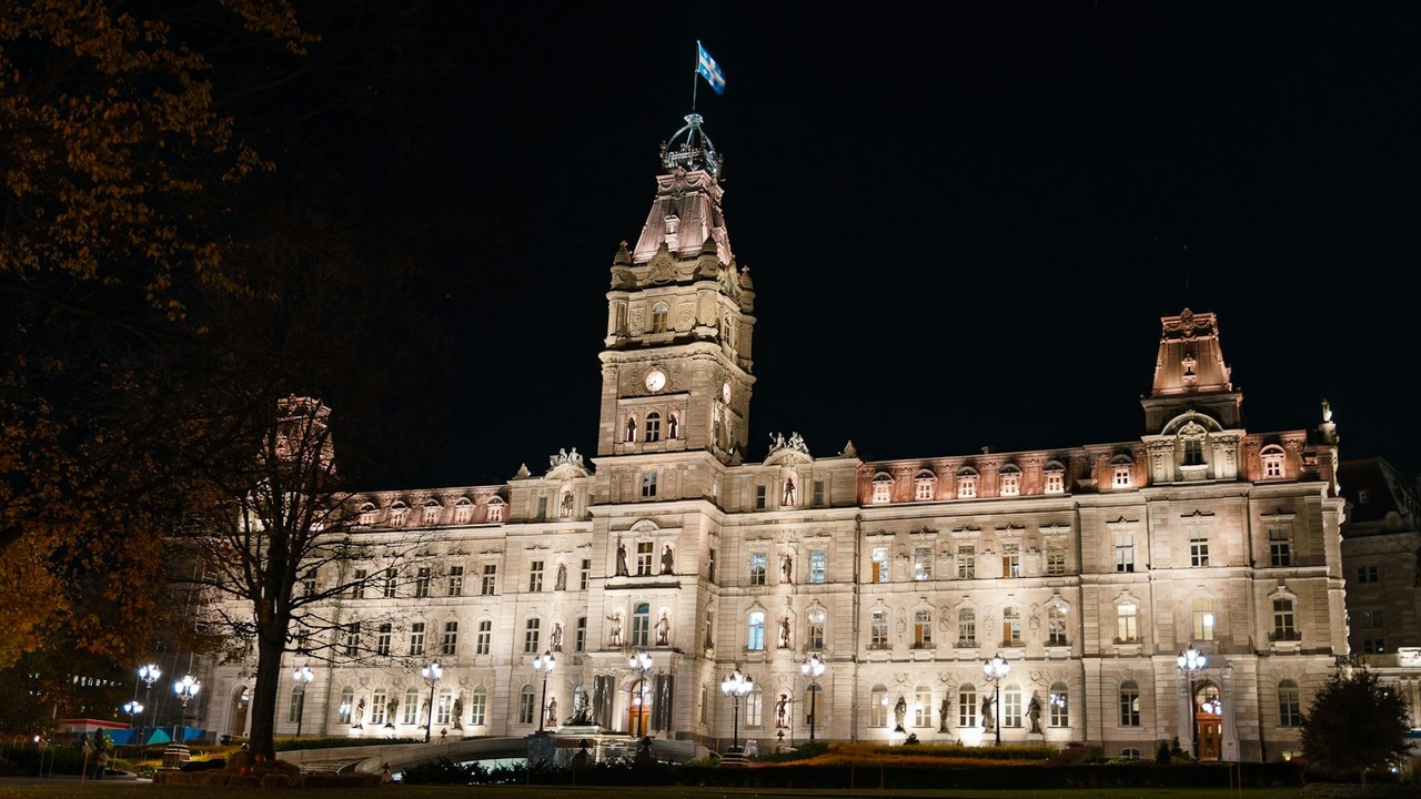 The Parliament Building in Québec City lit up at night, the Québec flag flying from its tower.