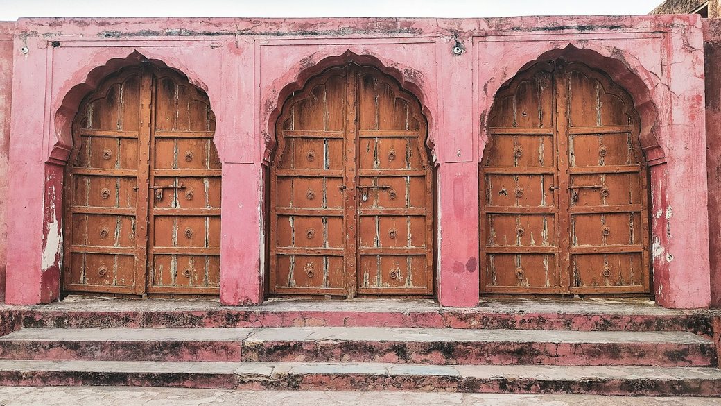 Three identical arched wooden doors side by side in a weathered pink wall.