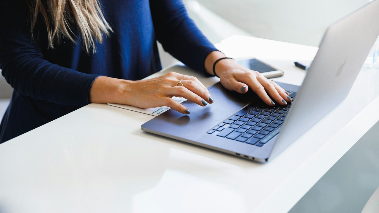 Hands typing on a laptop at a white desk.